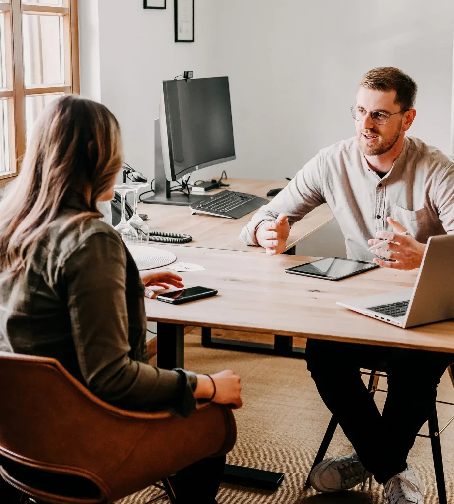 Lukas Kölzer (Steuerberater und Inhaber der Kölzer Steuerberatungsgesellschaft) mit einer Mandantin während einer Beratung. Auf dem Schreibtisch stehen Laptop und Tablet.